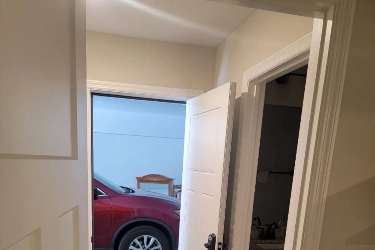 This image captures the private entrance to the apartment, showing an open door that leads directly from the garage into a cozy, welcoming space. A car is visible in the garage, emphasizing the direct and independent access provided to residents. The wooden chair and practical setting highlight the ease of entry and the absence of shared living space beyond the garage.