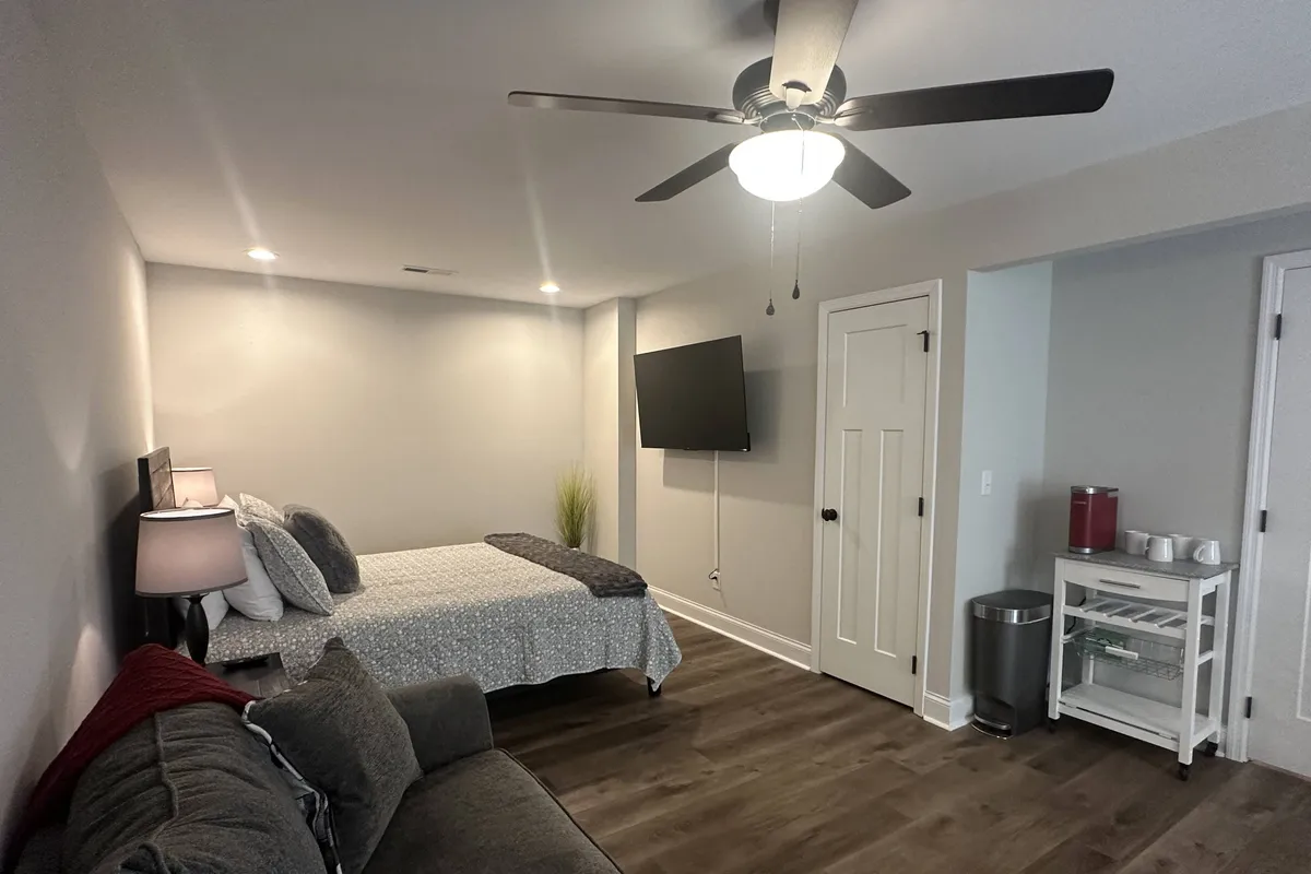 A restful bedroom and living combination, with a bed, sofa, TV, and side table arranged for both relaxation and entertainment. The setting is intimate and calm, underscoring the peace and solitude that comes with entirely private quarters.