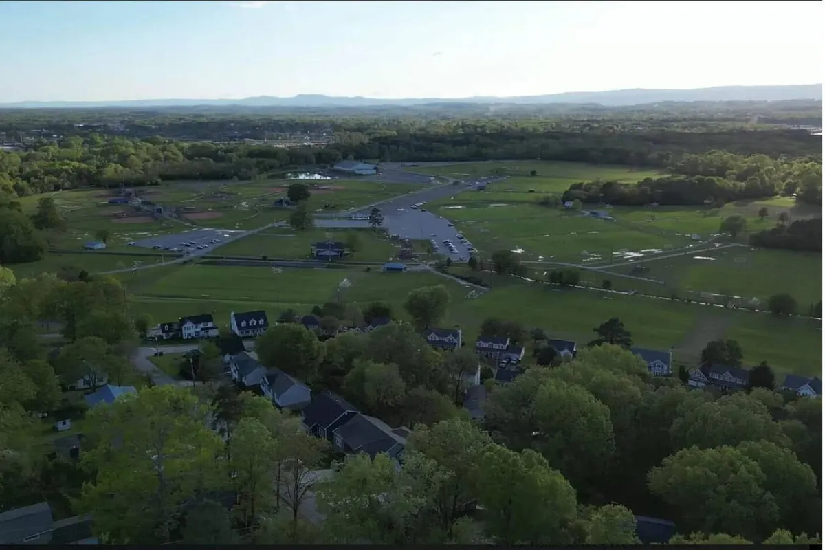A peaceful neighborhood scene with open green fields, community homes, and distant mountains under a bright sky. The area feels welcoming and open, suitable for relaxation after a workday.