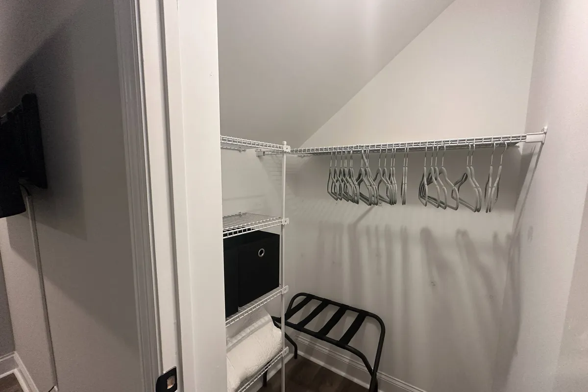 A practical closet scene complete with shelves, hangers, a storage box, and a foldable stool, all arranged for easy organization and ample storage. The image radiates a sense of order and readiness for guests to settle in for an extended period.
