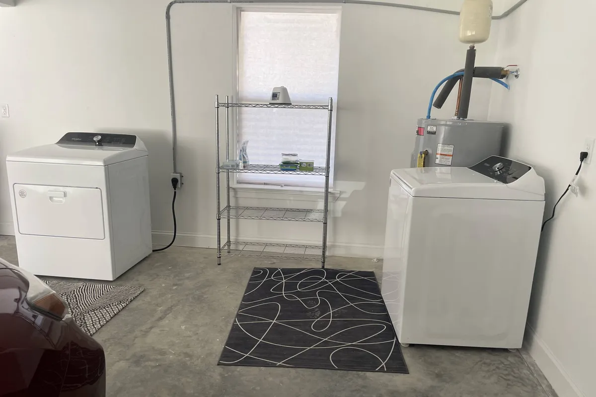 A tidy laundry nook featuring a washer, dryer, shelving, and a window, illustrating the convenience of in-unit laundry and organized storage for supplies. The practical layout promotes ease and independence during longer stays.